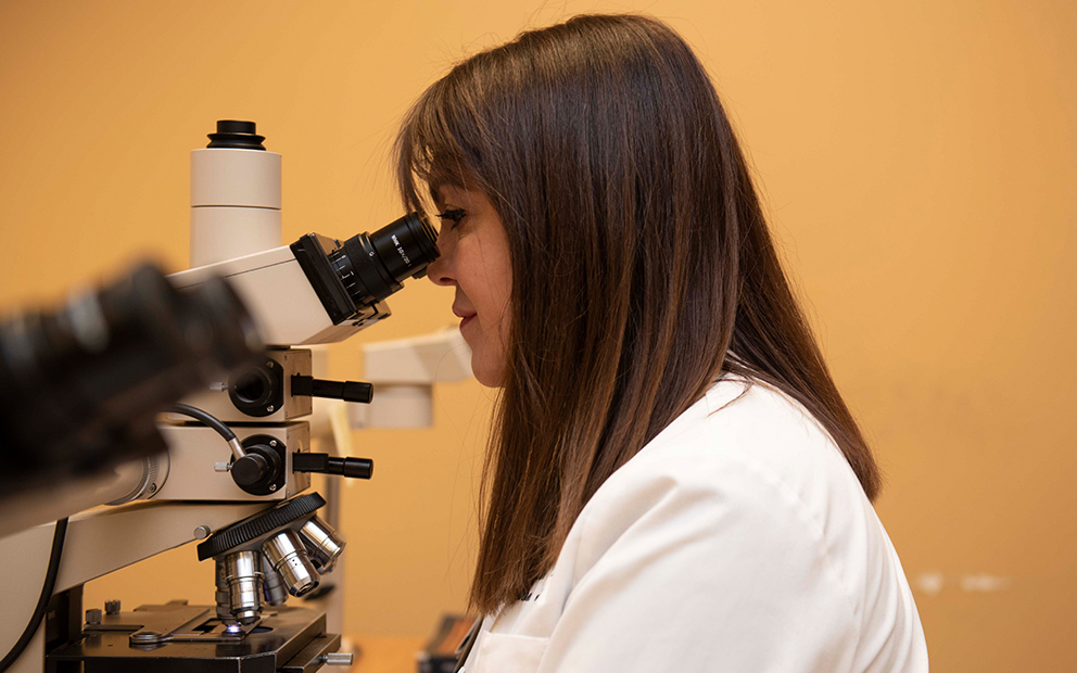 Woman in lab coat looking into a microscope