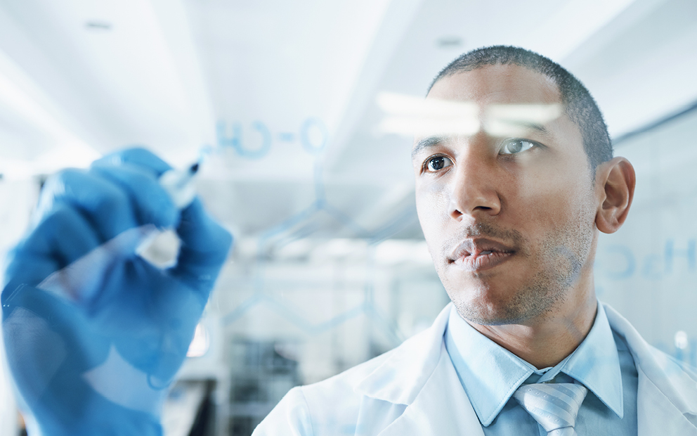 Man in lab coat writing a formula on white board