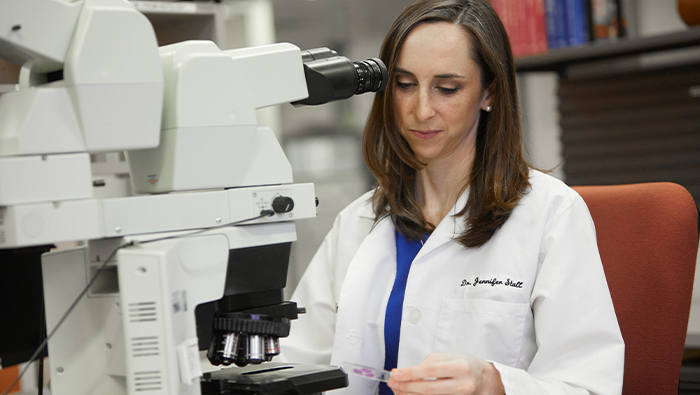 Woman in a lab with a microscope looking down at a slide