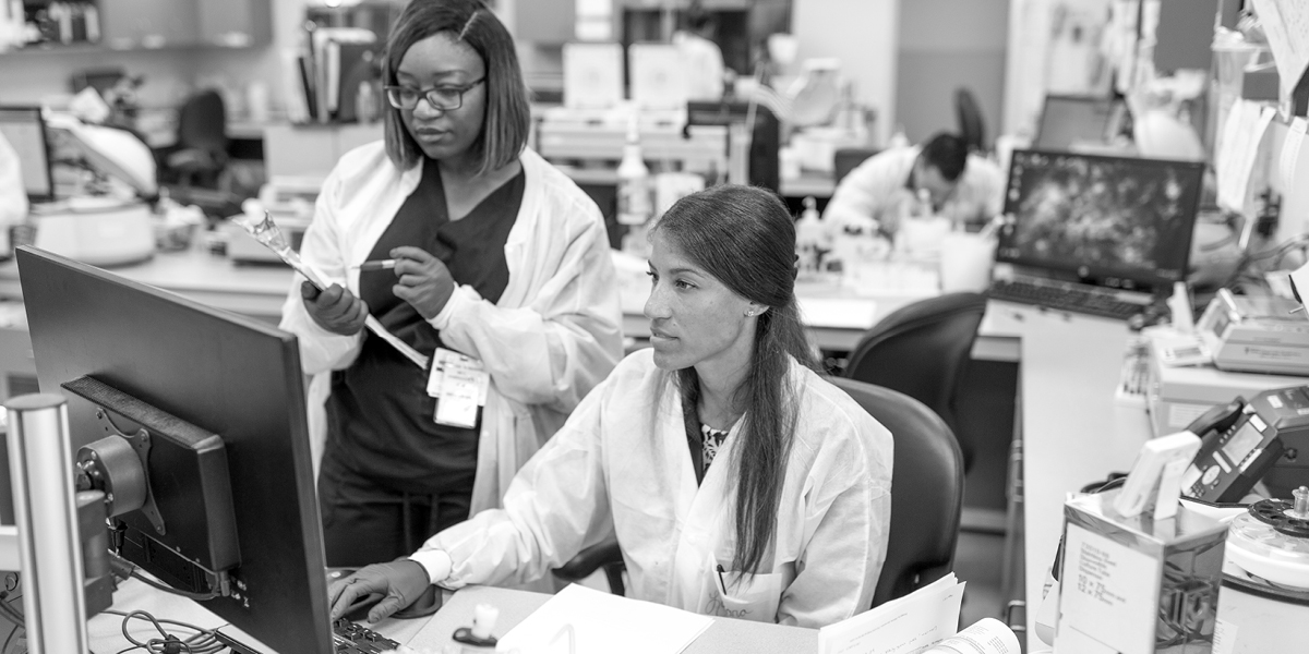 Two woman in lab coats looking at a monitor